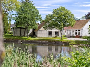 En kanal med byggnader på ena sidan, en liten bro och ett grönområde med träd.