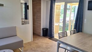 Een kamer met een bank, een eettafel met stoelen, een klein rond tafeltje met een afstandsbediening, en een glazen schuifdeur naar een buitenruimte.