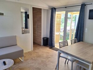 Ein Zimmer mit einer Couch, einem Esstisch mit Stühlen, einem kleinen runden Tisch mit einer Fernbedienung und einer Schiebeglastür, die zu einem Außenbereich führt.
