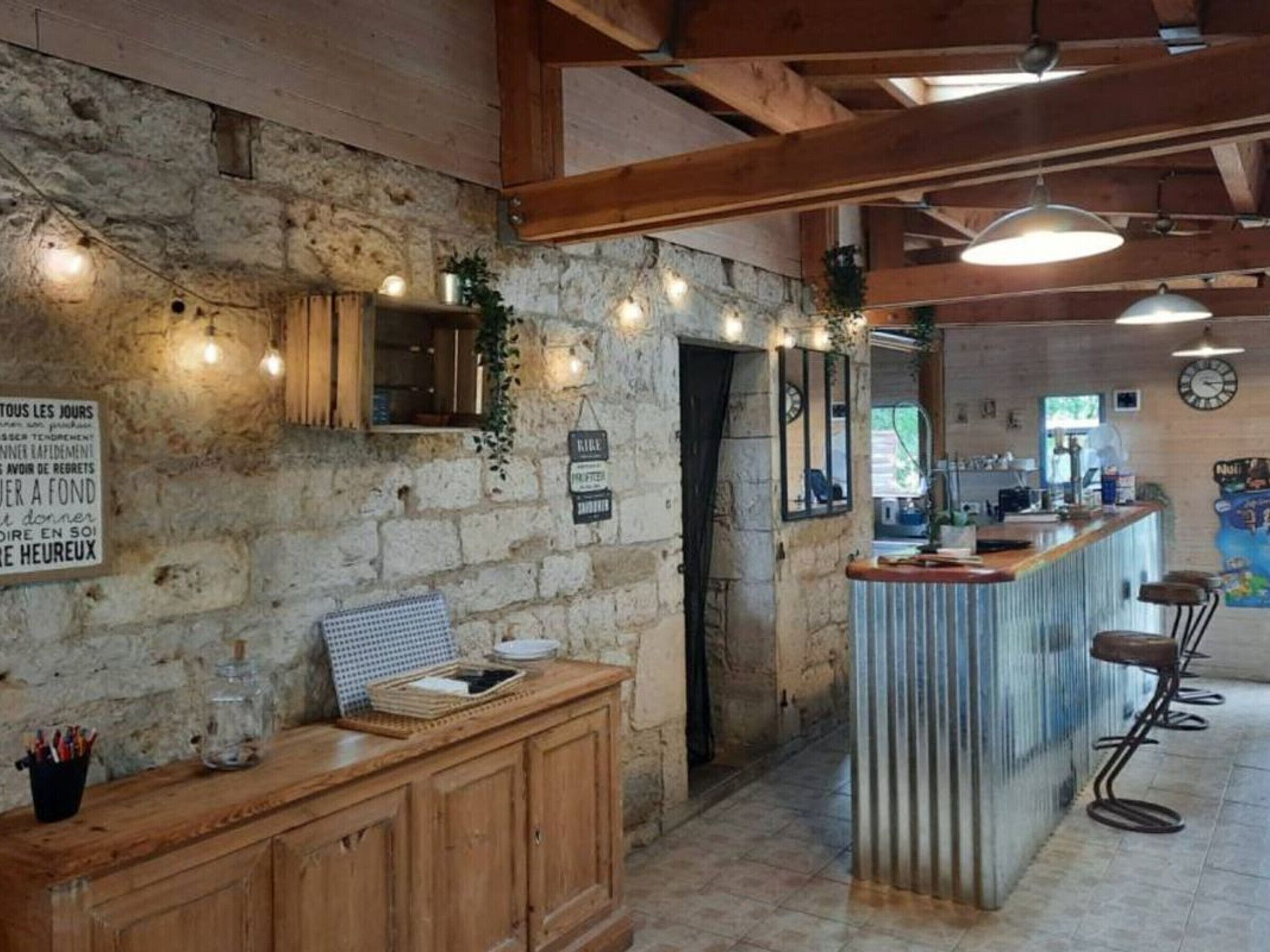A rustic interior with exposed stone walls, wooden beams, a bar area with stools, and a sign with French text.