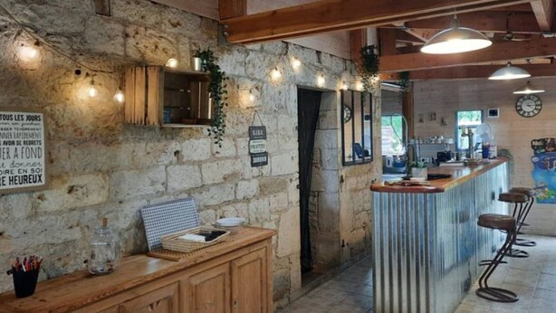 Een rustiek interieur met zichtbare stenen muren, houten balken, een bar met krukken, en een bord met Franse tekst.