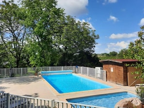 A rectangular swimming pool with a white fence surrounding it, a wooden building to the right, and trees in the background. - Comfortable mobile home with terrace - 4 guests (Rocamadour)