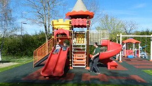 Un patio de juegos con un tobogán, una estructura para escalar y una casita roja y amarilla.