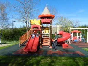 A playground with a slide, climbing structure, and a red and yellow playhouse. - Mobile home with terrace - 2 guests (Rocamadour)