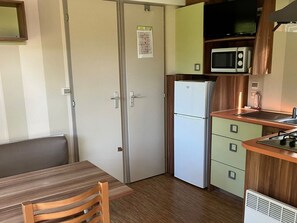 Eine kompakte Küche mit Kühlschrank, Mikrowelle und Herd. Es gibt einen Esstisch mit Stühlen und ein kleines Fenster.