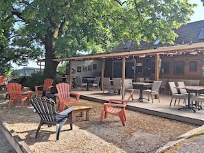 Ein Sitzbereich im Freien mit Adirondack-Stühlen und Tischen, einer Pergola und einem Gebäude mit Ziegeldach.