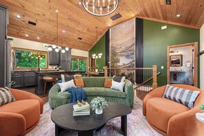 A spacious living area with a green sofa, orange armchairs, a coffee table, and a kitchen in the background. - Blowing Rock Getaway | Hot Tub, Sauna & Theatre (Blowing Rock)