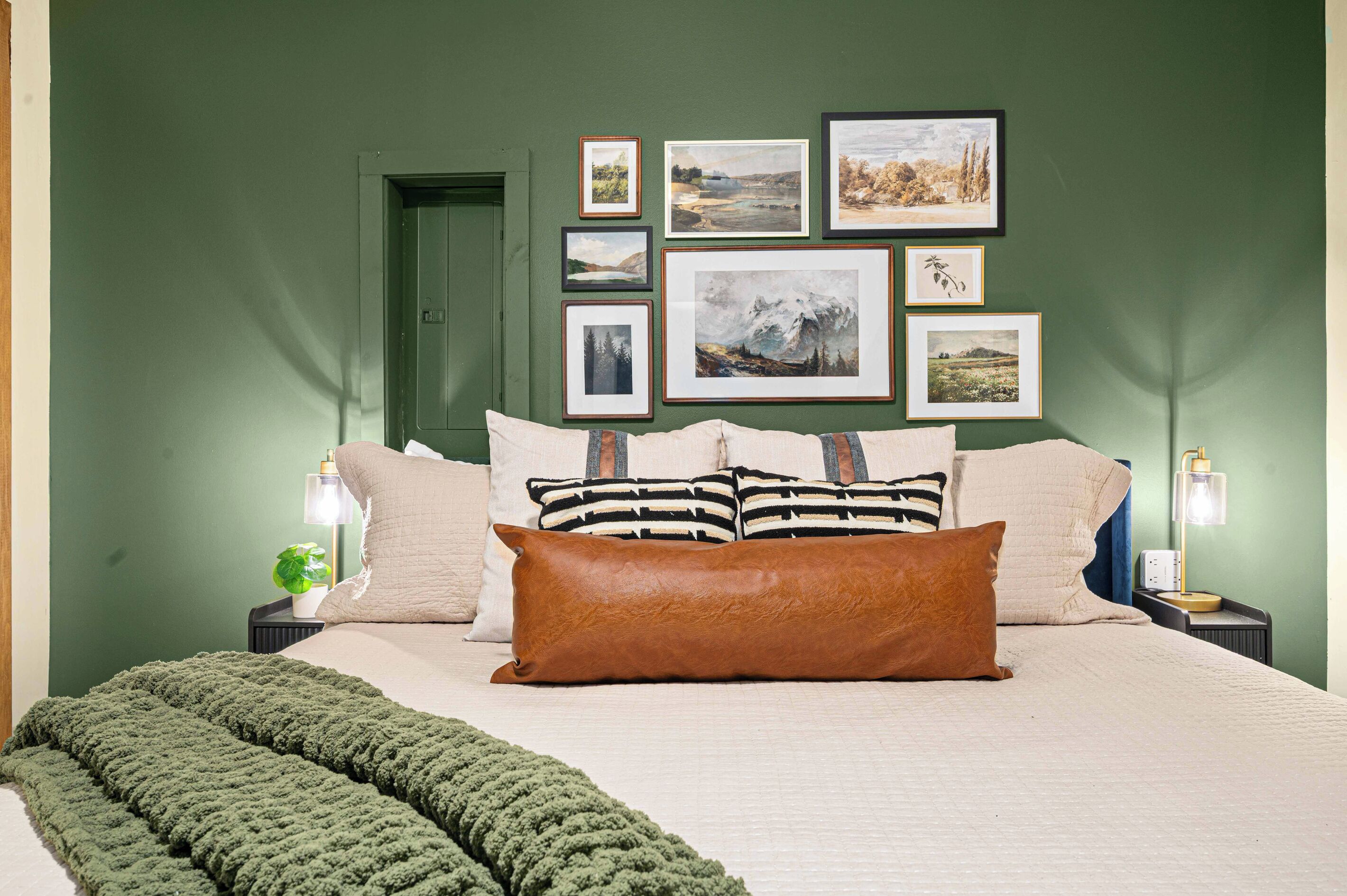 A bedroom with a bed, pillows, a green wall, framed pictures, and bedside lamps.