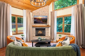 Ein gemütliches Wohnzimmer mit Kamin, zwei Sesseln, einer Couch und einem an einer Steinwand befestigten Fernseher.