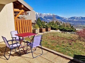 A patio with a table and chairs, wooden deck, and a view of snow-capped mountains. - Cozy apartment, pets welcome - 5 guests (Saint-Michel-de-Chaillol)