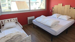 Een slaapkamer met twee bedden, een raam met uitzicht op gebouwen, en een rode wand.