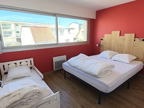 Ein Schlafzimmer mit zwei Betten, einem Fenster mit Blick auf Gebäude und einer roten Wand.