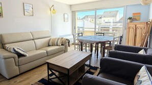 Een woonkamer met een bank, een bijzettafeltje en een eettafel met stoelen. Er is een raam met uitzicht op gebouwen.