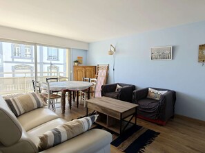Ein Wohnzimmer mit einer Couch, einem Couchtisch, einem Esstisch mit Stühlen, einem Holzkabinett und einem großen Fenster.
