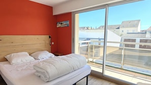 Een slaapkamer met een groot raam, een houten hoofdbord en uitzicht op gebouwen.