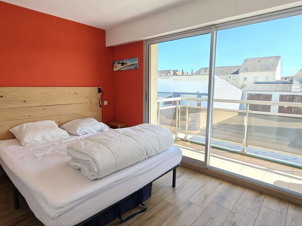 Quarto com uma janela grande, cabeceira de madeira e vista para prédios.