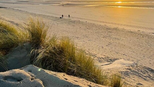Een strand met duinen en een zonsondergang.