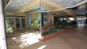Un espacio interior moderno con paredes de vidrio, un mural en el techo y una planta central con vegetación.