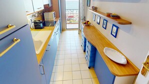 Una cocina estrecha con armarios azules, una encimera de madera y vistas al exterior.