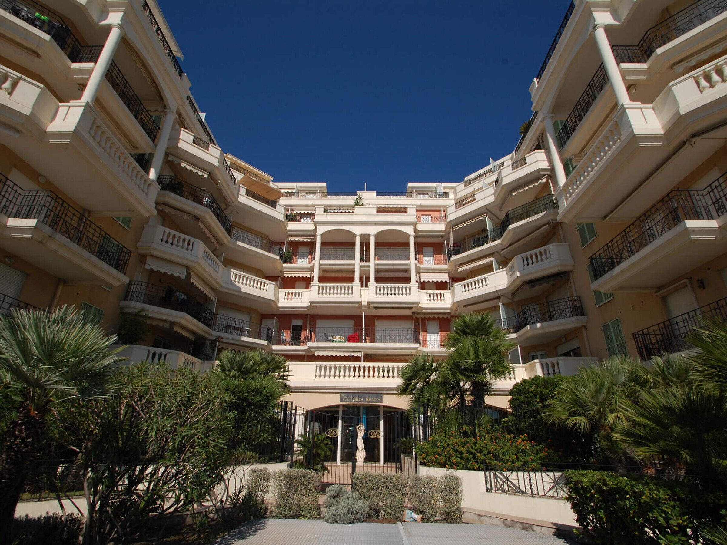 A multi-story hotel with a central courtyard, balconies, and a sign reading "VICTORIA BEACH".