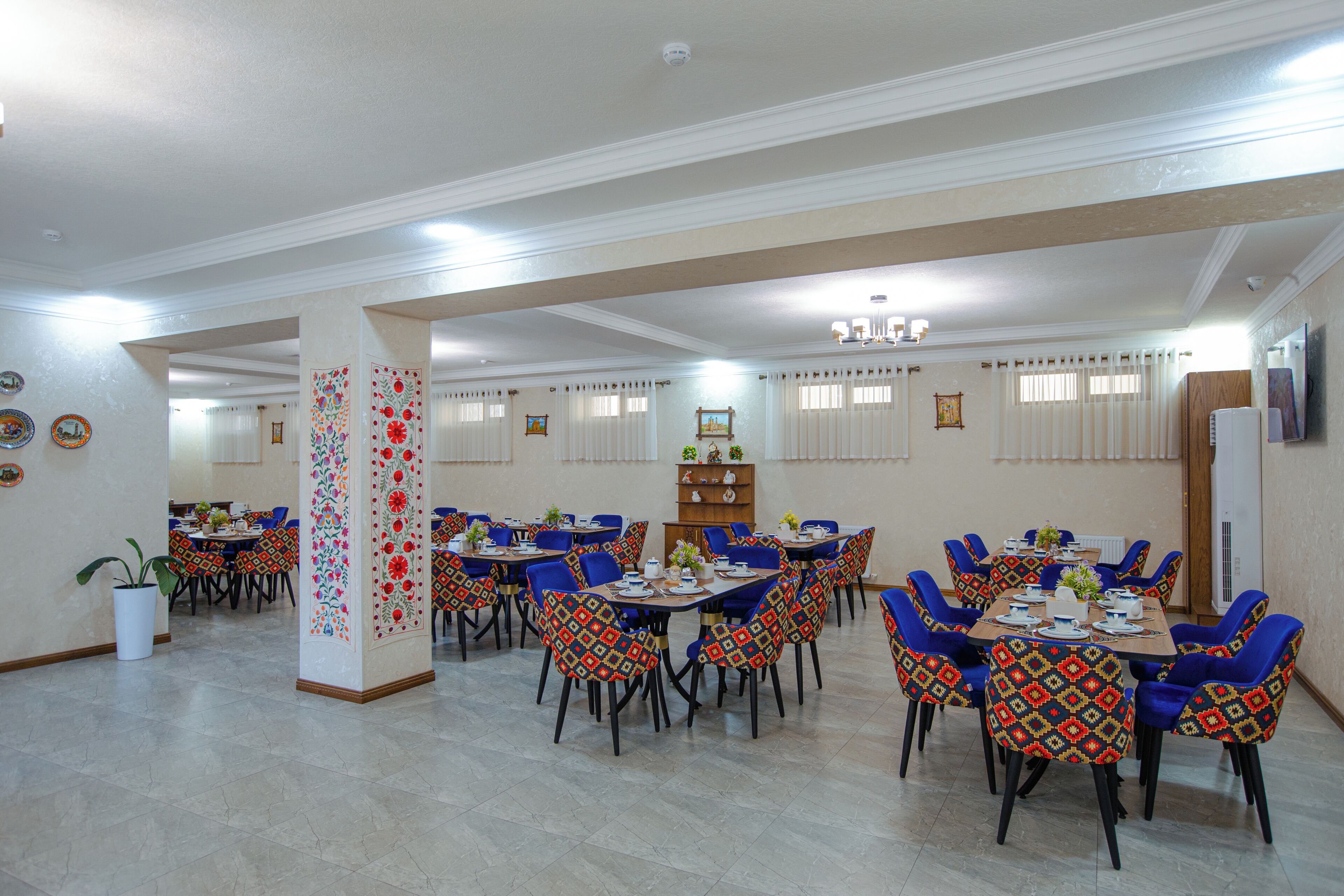 Uma área de refeições com várias mesas e cadeiras, um pilar decorativo central e um teto com iluminação embutida.