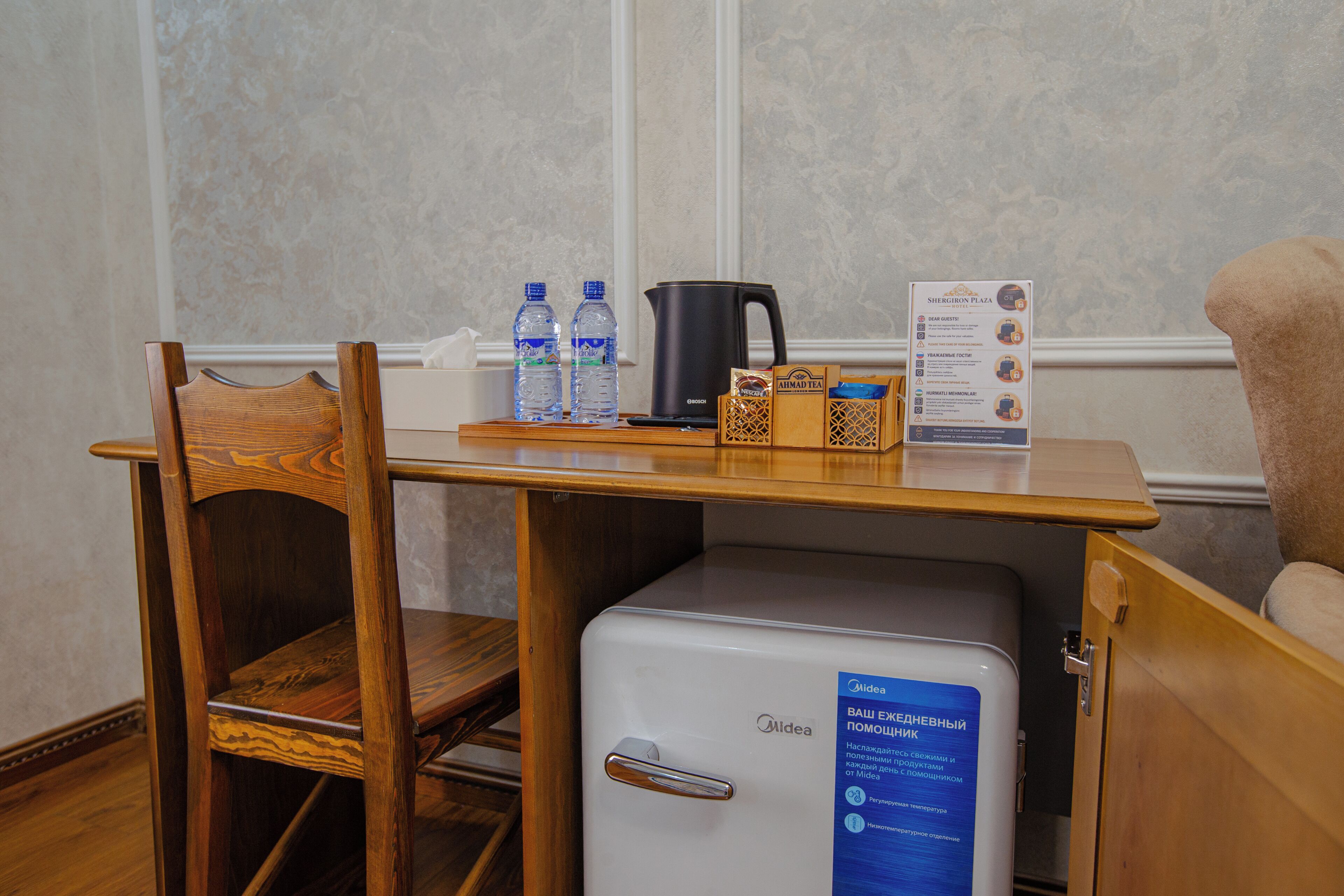 Una pequeña mesa de madera con un refrigerador blanco, una cafetera negra y dos botellas de agua.