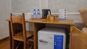 A small wooden table with a white refrigerator, two water bottles, a black coffee pot, and a tea box. - Shergiron Plaza (Bukhara)