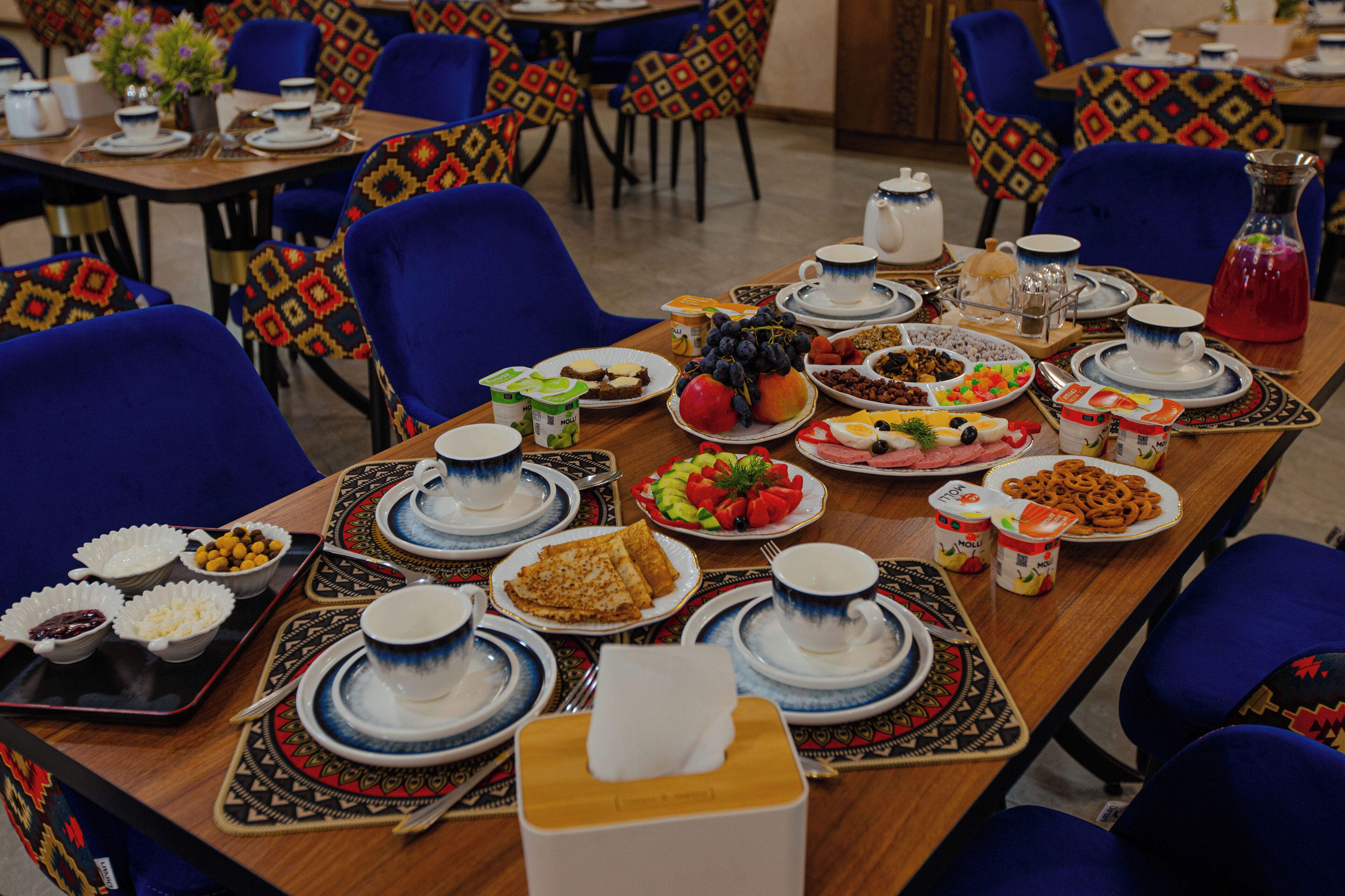 A dining table set with various dishes, plates, and utensils, surrounded by blue chairs.