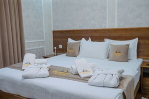 A neatly made hotel bed with towels and a blanket, a wooden headboard, and a nightstand with a lamp. - Shergiron Plaza (Bukhara)