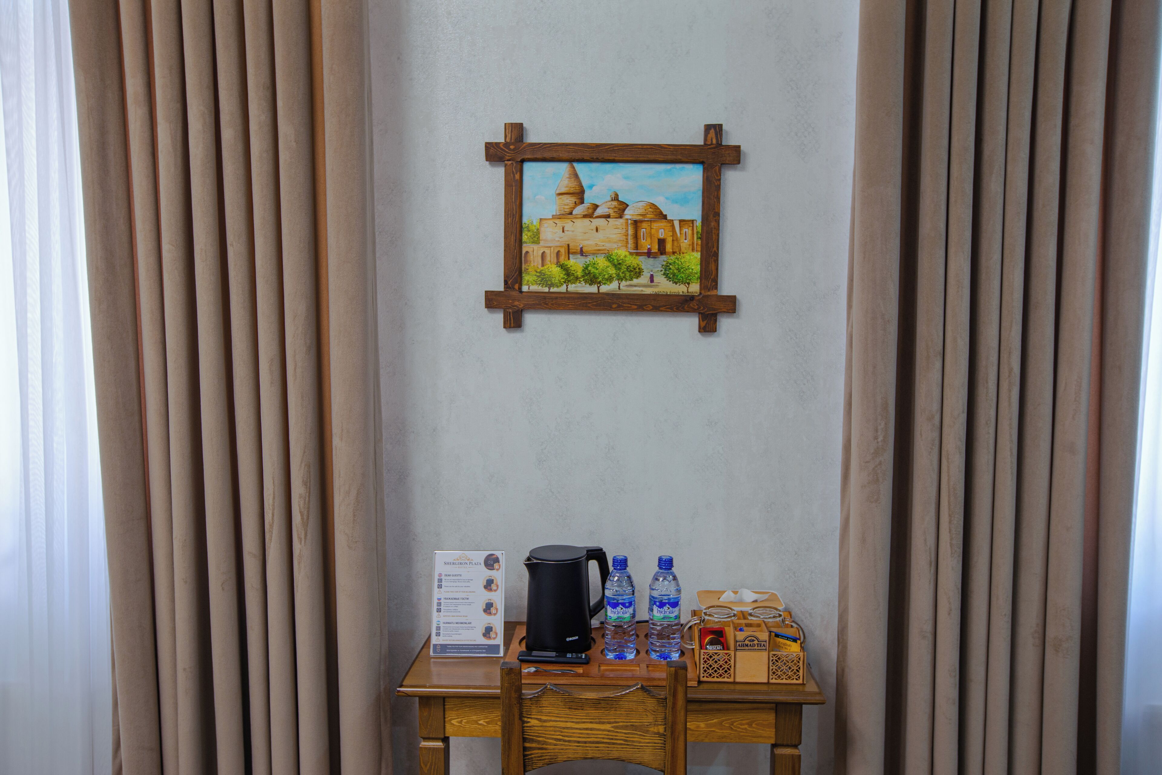 Una habitación con un cuadro de un edificio, una mesa con un hervidor, botellas de agua y un cartel.
