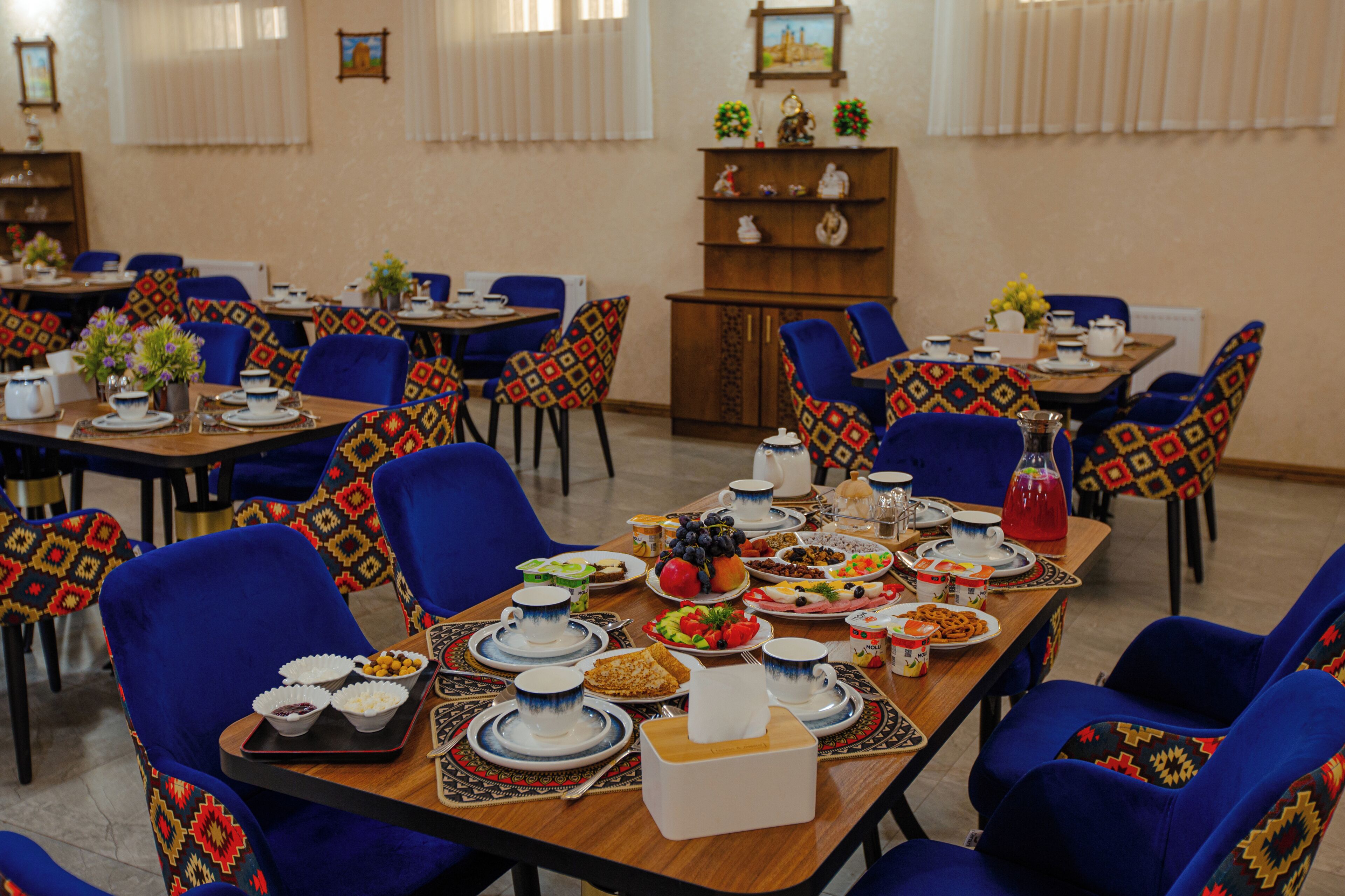 A dining area with multiple tables set for a meal, chairs with patterned upholstery, and a variety of dishes and drinks on the tables.