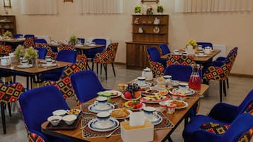 A dining area with multiple tables set for a meal, chairs with patterned upholstery, and a variety of dishes and drinks on the tables.