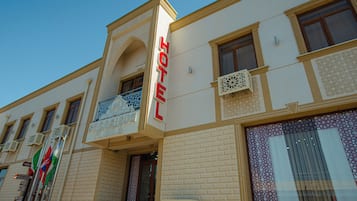 Un hôtel avec une enseigne bien visible, des balcons ornés de motifs complexes en treillis et un ciel dégagé.