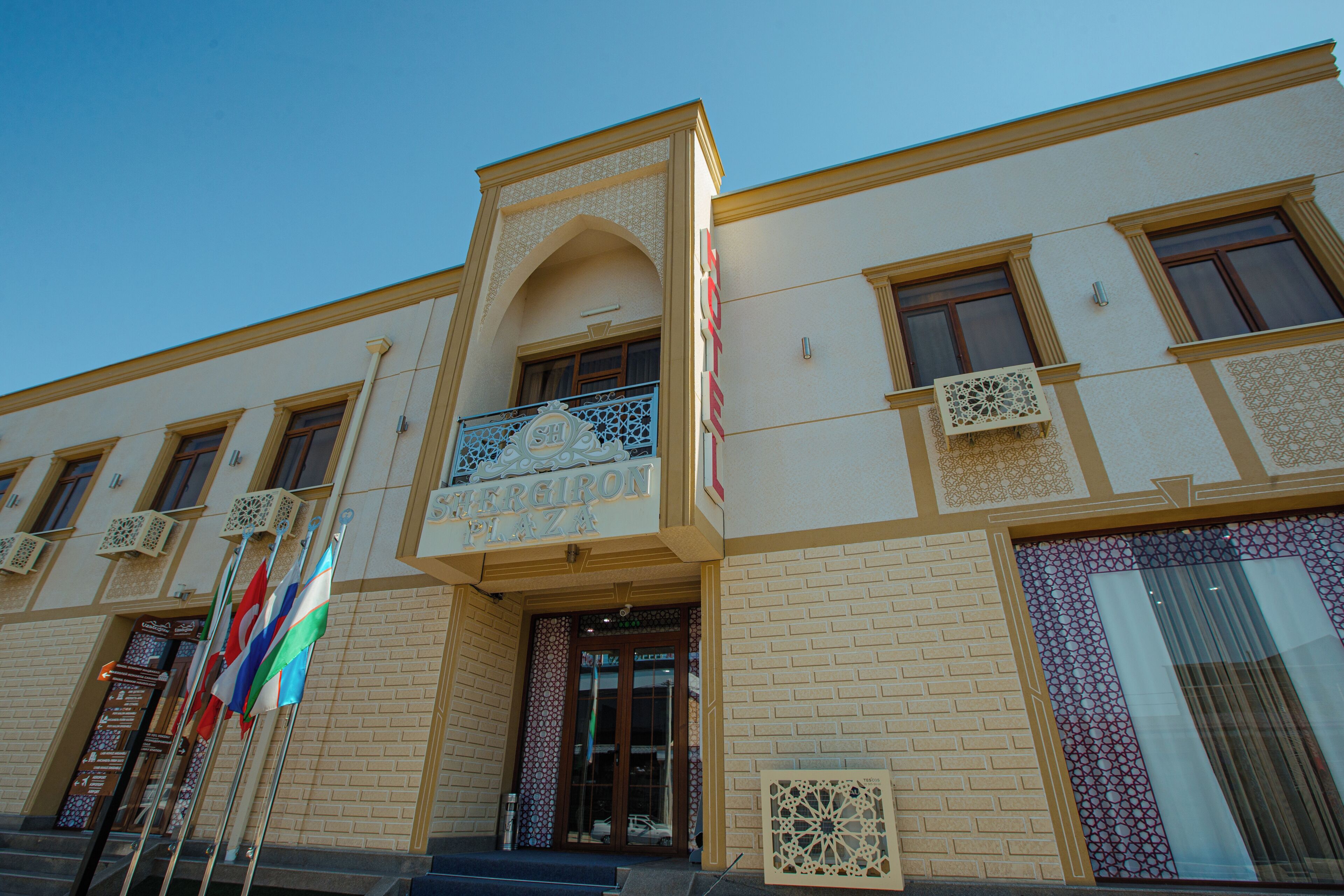 A building with a sign reading 'Sergion Plaza,' featuring a prominent entrance with a glass door, multiple windows, and decorative patterns on the facade.