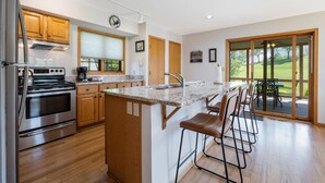 Een moderne keuken met houten kastjes, een roestvrijstalen oven, een granieten aanrecht en een bar met krukken.