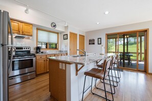 A modern kitchen with wooden cabinets, a stainless steel oven, a granite countertop, and a bar area with stools. - WV11 - An Eagle Ridge Resort & Spa Rental with Full Resort Amenities and Owners Club Access! (Galena)