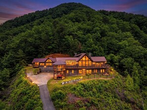 A large, multi-story lodge with a prominent central tower, surrounded by dense forest. - Private Mountain Resort | Indoor Pool, Theater & Sleeps 30 (Sevierville)