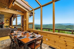 A wooden interior with a dining table set for four, large windows offering a mountain view, and a fireplace. - Private Mountain Resort | Indoor Pool, Theater & Sleeps 30 (Sevierville)