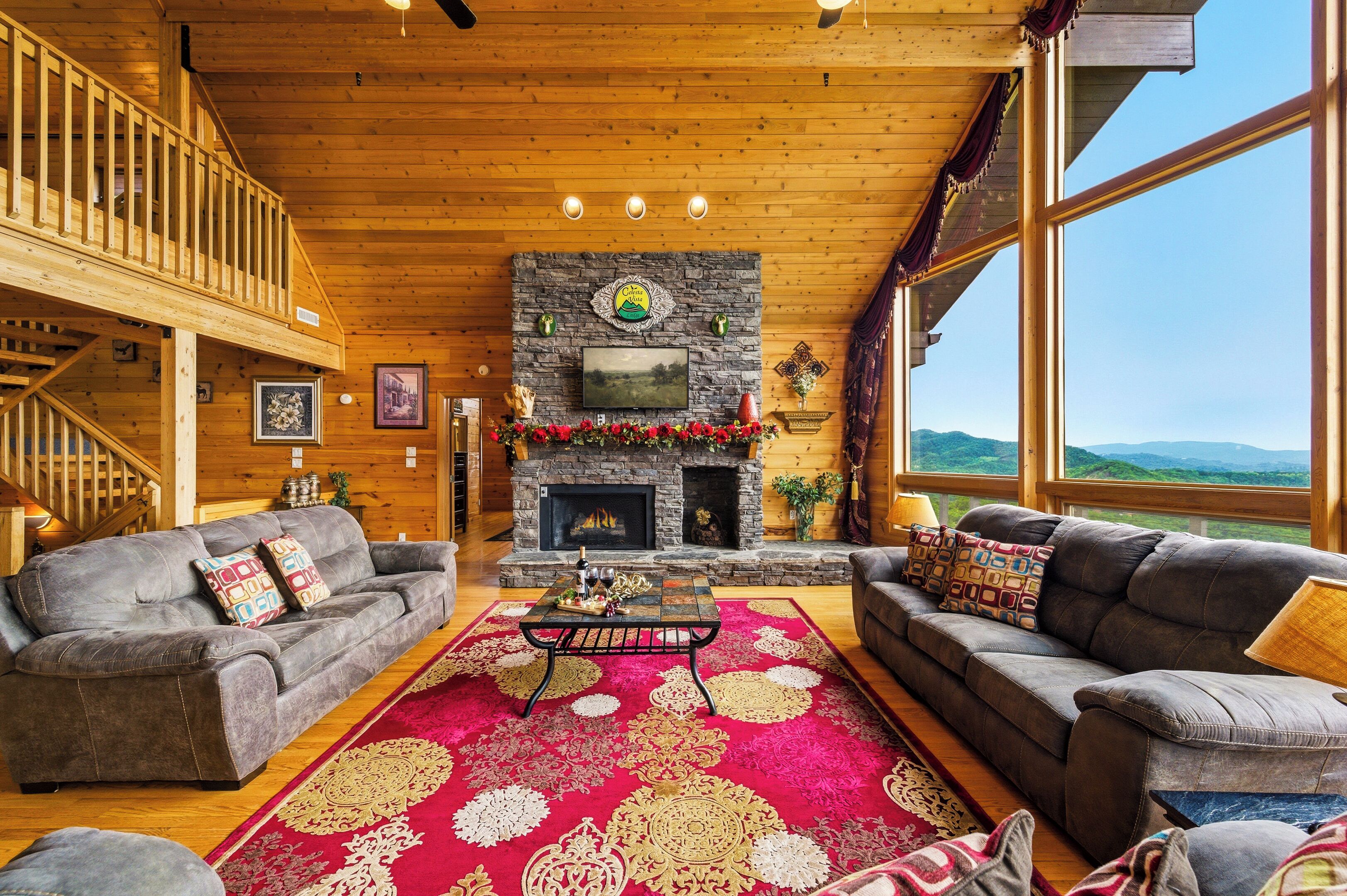 A spacious living room with a stone fireplace, two sofas, a coffee table, and a large window offering a mountain view.