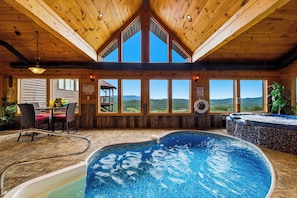 A wooden cabin with a hot tub, a dining area, and large windows offering mountain views. - Private Mountain Resort | Indoor Pool, Theater & Sleeps 30 (Sevierville)