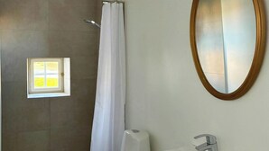 Un baño con inodoro, lavamanos, ducha y un ventanal pequeño.