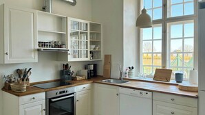 Una cocina moderna con armarios blancos, horno empotrado, lavavajillas y ventana con vistas a un jardín.