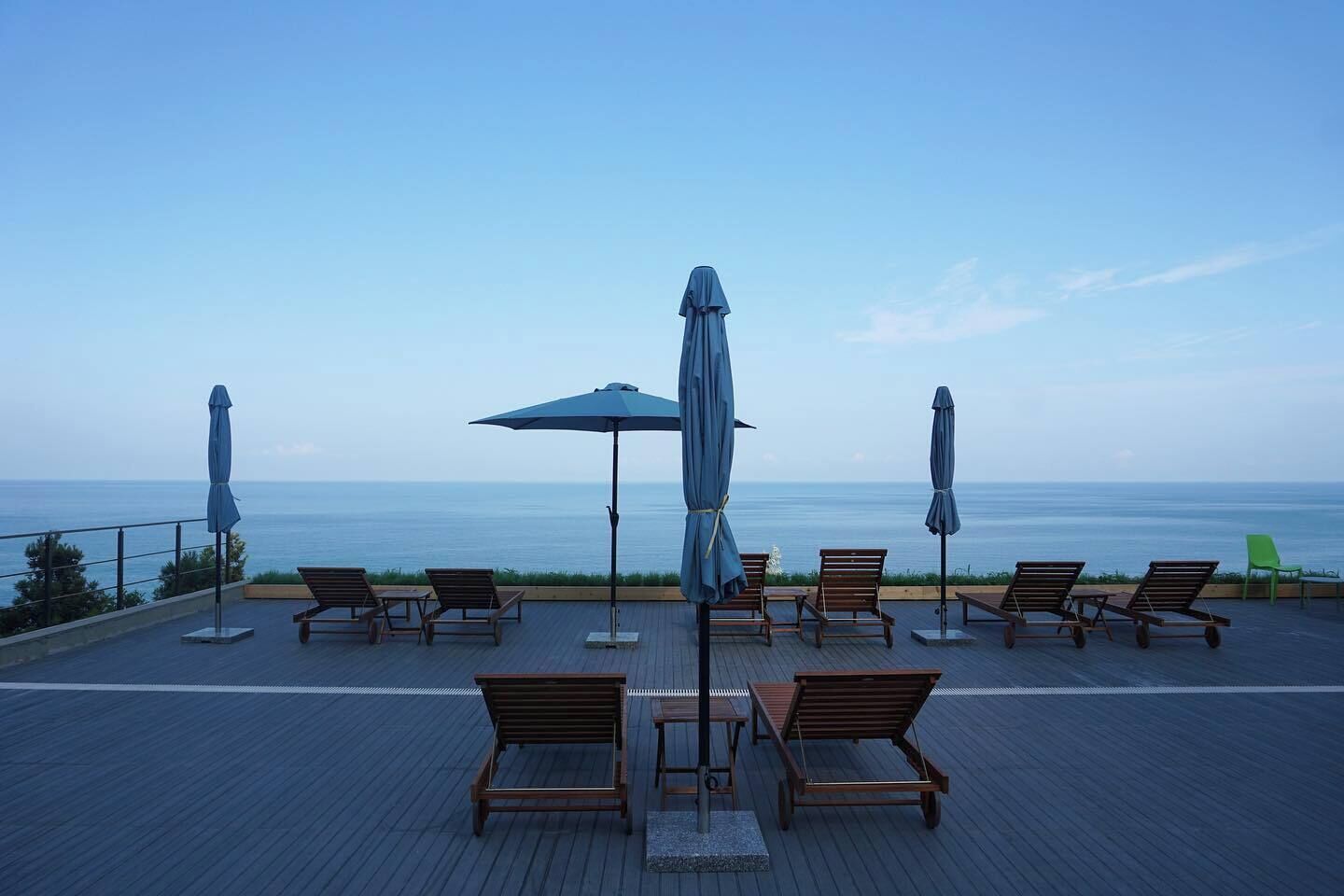 A rooftop terrace with wooden lounge chairs and umbrellas, overlooking the sea.