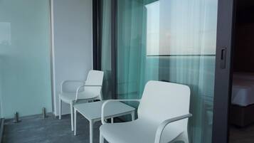 A modern room with a glass door, white chairs, a small table, and a bed with a white cover.