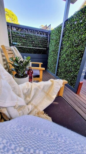 A cozy outdoor seating area with a cushioned chair, a small table, and a potted plant.