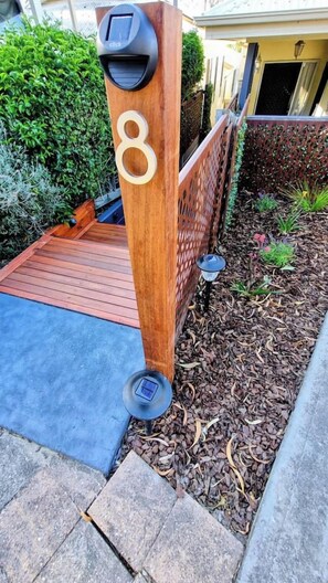 Un buzón de madera con el número 8, una puerta metálica y un pequeño jardín con acolchado y plantas.