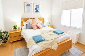 Un dormitorio ordenado con una cama, mesitas de noche, una ventana y una planta en maceta.