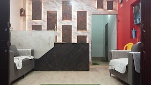 Zona de recepción con un mostrador de mármol, dos sofás con mantas, una pared roja y una puerta que da a otra habitación.