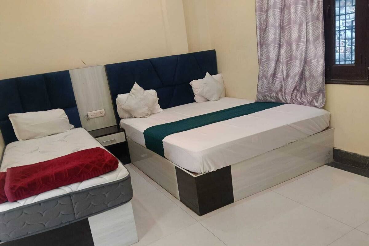 Una habitación de hotel con dos camas, una mesita de noche, una ventana con cortinas y piso de baldosas.
