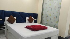 Una cama bien hecha con colchón blanco y manta roja, cabecera azul y mesita de noche con lámpara.